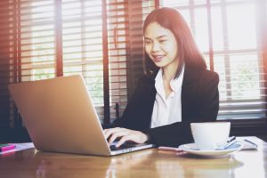 soft focus of woman working on laptop on wooden desk in office in morning light. Managing Email