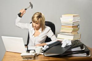 Disorganised and angry business lady hitting a laptop with a hammer. She needs to get organised to reduce stress.