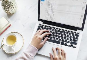 Optimise Microsoft Outlook. Laptop with the hands of a person typing on a desk with a cup of tea sitting on the desk also.