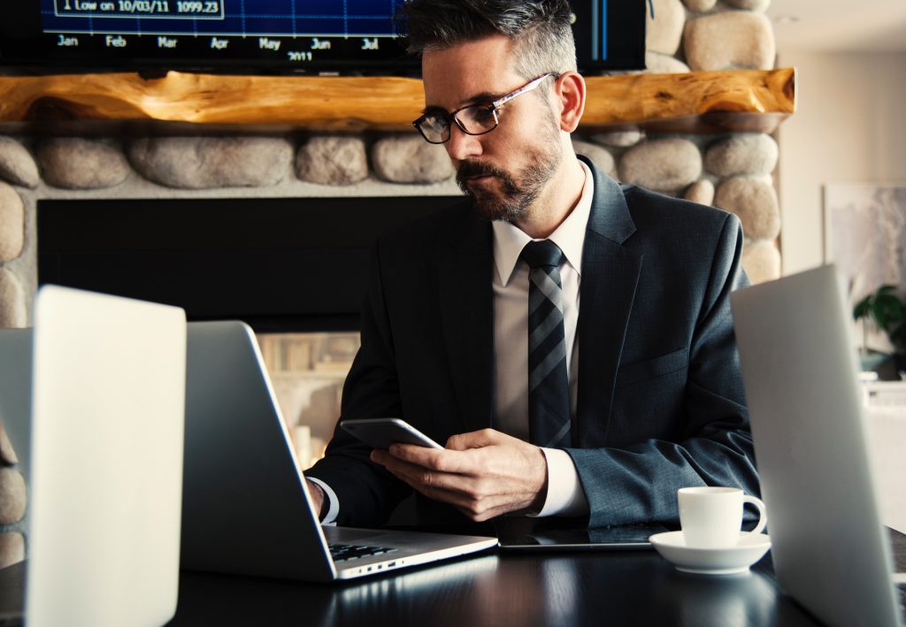 Business man typing on a laptop whilst holding a phone. 4 steps to a clean and stress-free Email Inbox.