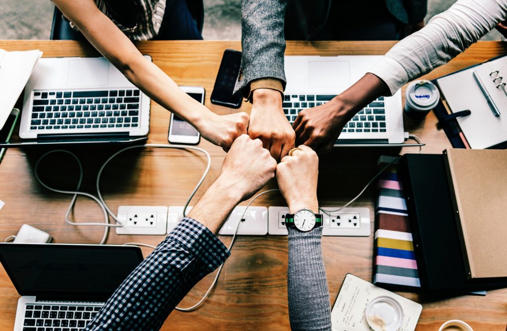 Share OneNote to boost your productivity. 5 People Clenching their fists together over Laptops Computers.