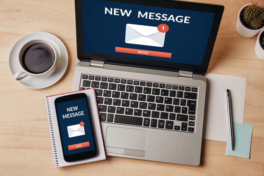 New email notification concept on laptop and smartphone screen over wooden table. 