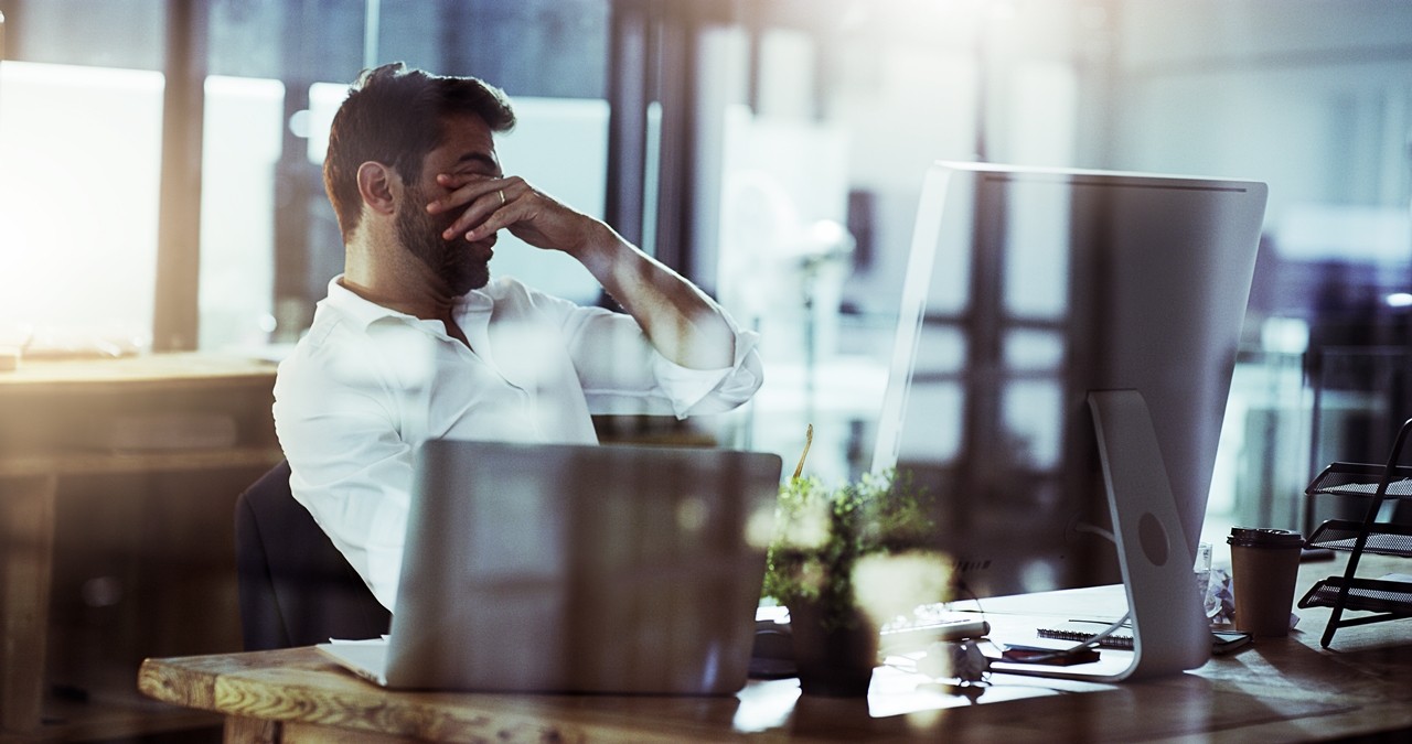 young businessman looking stressed while working late in the office. Impact of technology in the workplace.