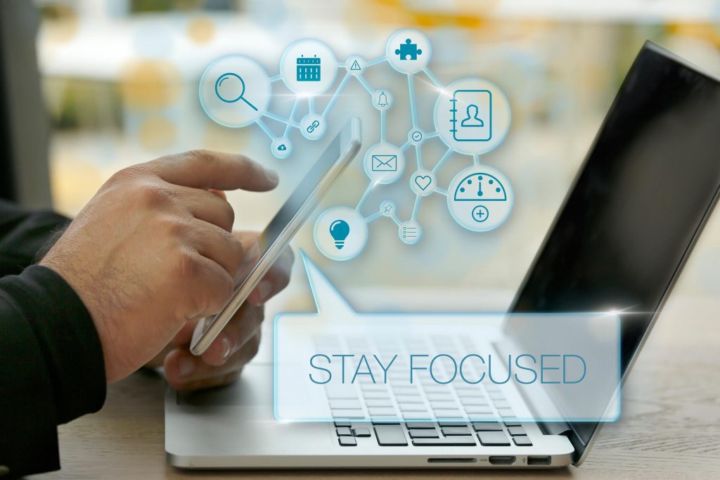 Man using phone above Laptop with the words stay focused inserted as a call out.