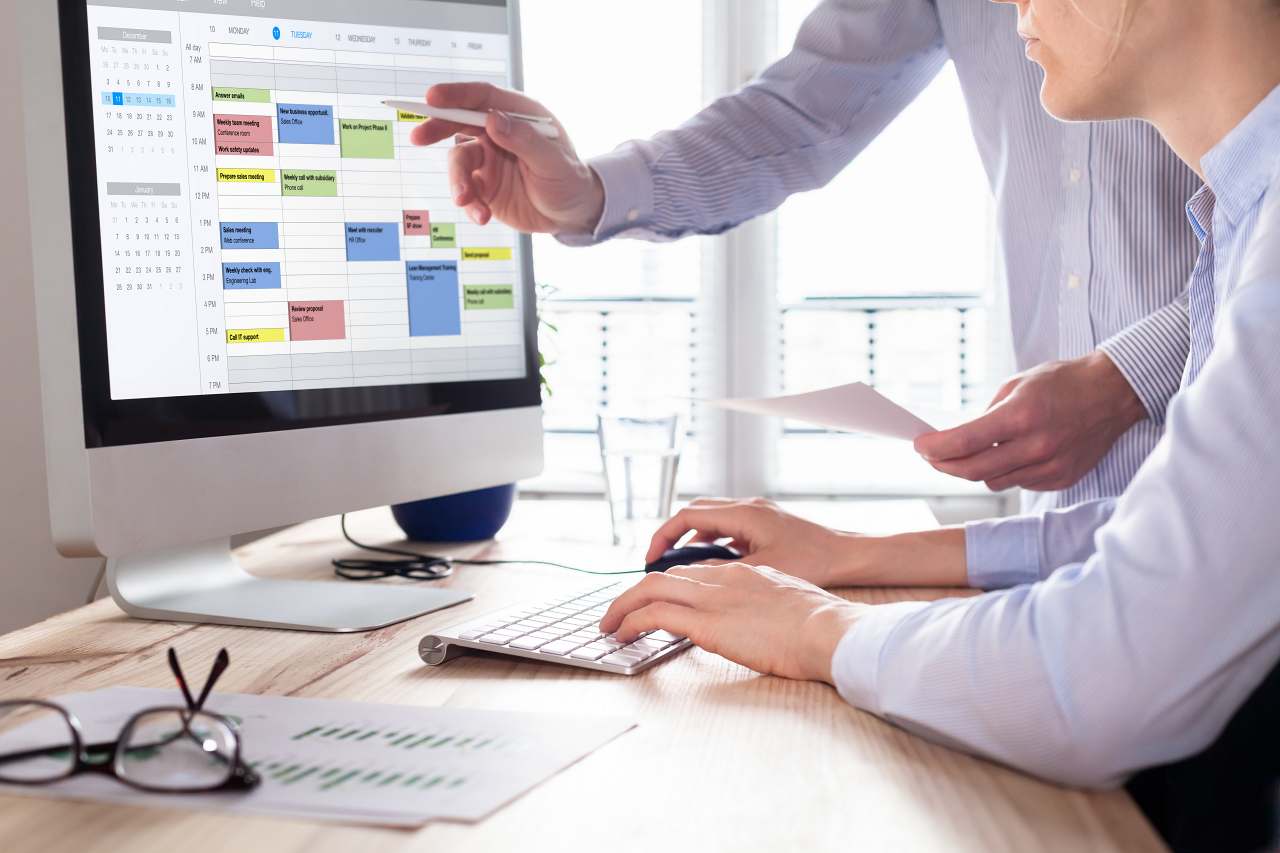 Two people behind a computer screen icalendar showing, trying to plan a meeting. Time blocking