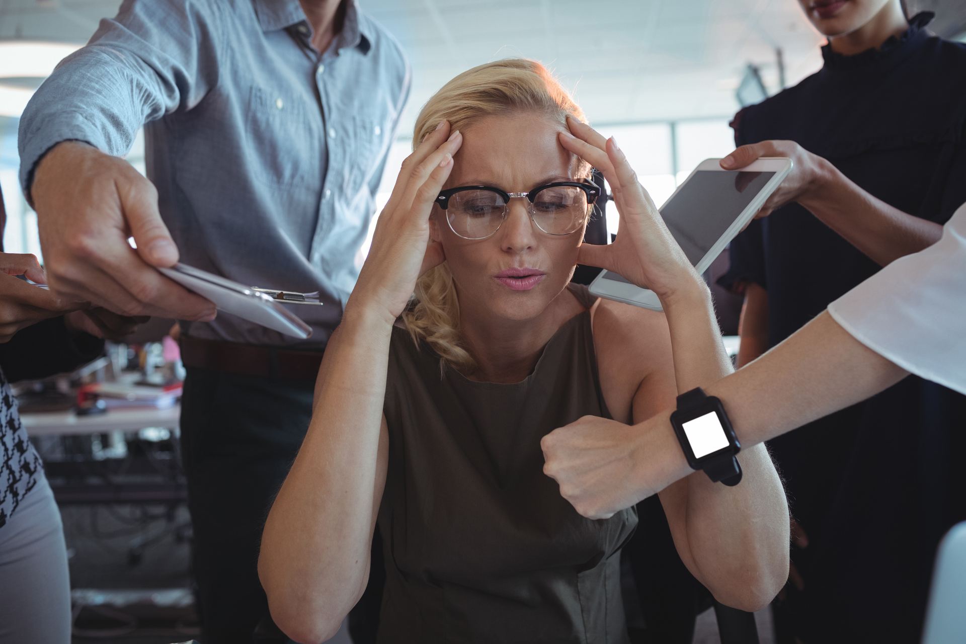 Frustrated businesswoman sitting amidst team holding technologies and competing priorities at office